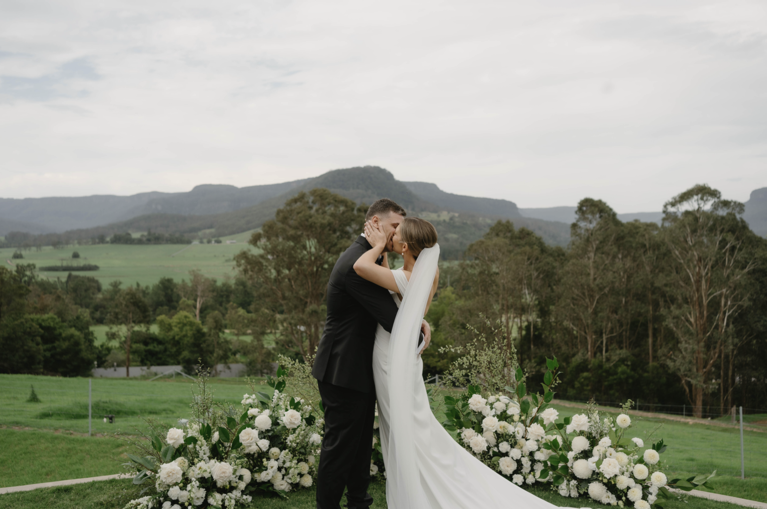 Couple kissing at the floral ceremony arch overlooking Kangaroo Valley